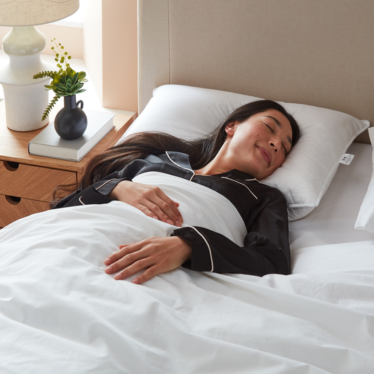 Woman sleeping peacefully in bed with white bedding and a nightstand.